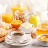 Un tavolo imbandito con croissant, caffè, succo d'arancia, frutta e marmellata, perfetto per delle bevande per colazione.