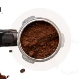 Macinatura caffè fine nel portafiltro, pronta per un espresso perfetto. Chicchi sparsi e logo Fusari.