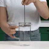 Mano che preme lo stantuffo di una french press di vetro, pronta per un caffè aromatico.