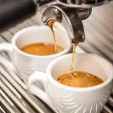 Due tazzine di caffè espresso vengono riempite da una macchina, ma il sapore bruciato del caffè rovina l'esperienza.
