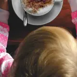 Bambini che gustano un caffè decaffeinato, con una tazza di cappuccino spolverato di cacao.