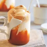 Un bicchiere di caffè freddo con schiuma cremosa e latte di mandorla, servito con una cannuccia.