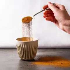 Mano versa polvere da un cucchiaio in una tazza. Forse è caffè solubile, ma fa male.