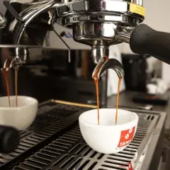 Due tazze bianche ricevono il prezioso liquido scuro, il caffè espresso, dalla macchina professionale.