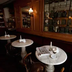 Un tavolino in marmo con un caffè, giornale e candela, in un antico caffè torinese.