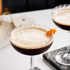 Due cocktail scuri con schiuma chiara, guarniti con scorza d'arancia. Un'idea per un caffè e succo d'arancia rivisitato.