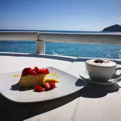 Un dolce con fragole e un caffè fumante, con il mare azzurro e un'isola all'orizzonte. Un momento di puro relax con un caffè al mare.
