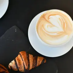 Un cappuccino con latte art a forma di cuore e croissant per una perfetta colazione al bar.