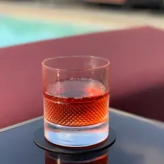 Un bicchiere di Sazerac, cocktail IBA, riposa su un tavolino vicino a una piscina.