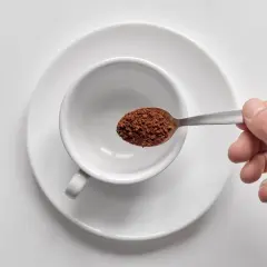 Mano che versa orzo café in una tazzina bianca.