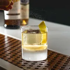 Un barista completa la negroni ricetta bar con una scorza di limone. Ghiaccio e liquore dorato in un bicchiere.