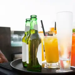Un cameriere serve un aperitivo originale: birre fresche e cocktail colorati su un vassoio.