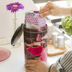 Mano inserisce pacchetto di caffè sottovuoto in un barattolo decorato. Freschezza garantita!