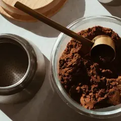 Caffè macinato in una ciotola di vetro, pronto per essere conservato. Un misurino dorato e una moka completano la scena, suggerendo come conservare il caffè al meglio.