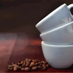 Tre tazzine bianche impilate, con chicchi di caffè tostati in primo piano. Immagina quanto contiene una tazzina di caffè.