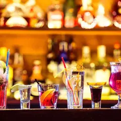 Varietà di cocktail principali colorati e rinfrescanti, guarniti con frutta e cannucce, su uno sfondo di bottiglie illuminate.