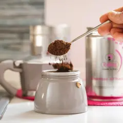 Un cucchiaino di caffè macinato cade nel bricco di una caffettiera, un ricordo di come si faceva il caffè prima della moka.