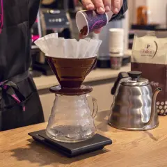 Preparazione di un caffè drip. Caffè macinato versato in un filtro, bollitore e sacchetti di caffè sullo sfondo.