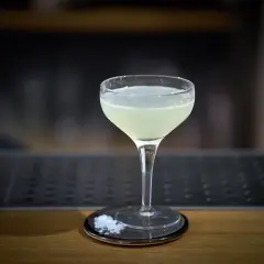 Un bicchiere di cocktail aspri, con sale grosso sul piattino, pronto per essere gustato.