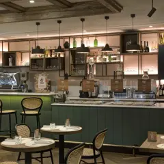 Interno di un locale moderno con bancone, macchine da caffè e tavoli. Un'atmosfera perfetta per gustare un ottimo caffè a Roma, famoso in tutto il mondo.