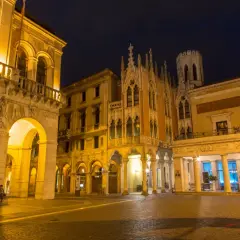 Edificio storico illuminato di notte a Padova, con archi e dettagli gotici. Un luogo che evoca il fascino di un **caffè storico Padova**.