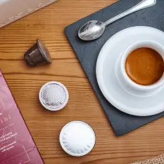 Vari tipi di caffè in capsule, una tazzina di espresso fumante e la confezione Rossini.