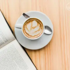 Un libro aperto e una tazza di caffè con schiuma, un invito al caffè illuminismo, su un tavolo di legno.