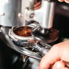 Macinatura caffè bar: polvere scura cade nel portafiltro, pronta per un espresso perfetto.