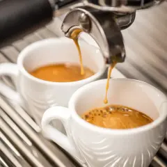 Due tazzine di caffè espresso vengono riempite da una macchina, ma il sapore bruciato del caffè rovina l'esperienza.
