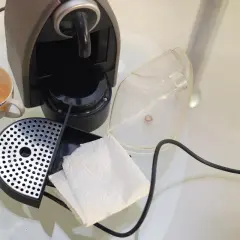 Macchina caffè bar smontata per pulizia: tazzina sporca, vaschetta raccogligocce, serbatoio trasparente e fazzoletti di carta.