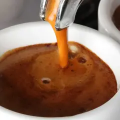 Un filo dorato di caffè caldo si riversa in una tazzina bianca, creando una crema invitante. Un buon caffè per iniziare la giornata.