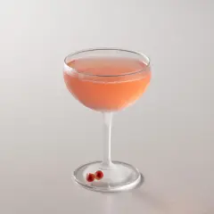 Cocktail rosa in coppa, perfetto per la tua bacardi cocktail ricetta. Due chicchi di melograno sul piattino.