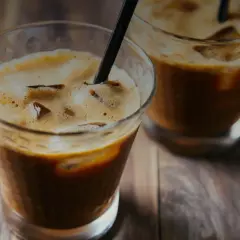 Due bicchieri di **cold brew** con ghiaccio e cannucce nere su un tavolo di legno.