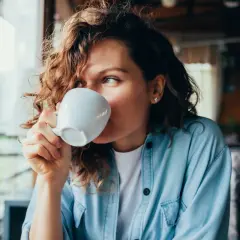 Donna con capelli ricci beve una tazza di caffè, un momento di relax con potassio naturale.