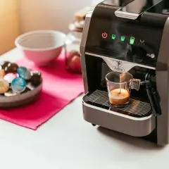 Macchina da caffè prepara un espresso. Accanto, una ciotola piena di capsule colorate, per scegliere se è meglio cialde o capsule.