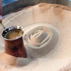 Un cezve di caffè turco viene preparato nella sabbia calda, creando un vortice invitante.