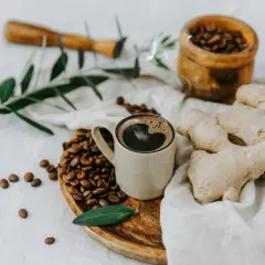 Tazza di caffè messicano fumante, chicchi tostati, zenzero fresco e un rametto d'ulivo su un panno di lino.