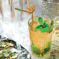 Un rinfrescante cocktail Italia, con menta e ghiaccio, accanto a ostriche gratinate e un flacone di profumo Chanel.