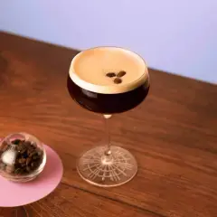 Un elegante cocktail espresso martini, con chicchi di caffè a guarnire, accanto a una piccola sfera di vetro piena di chicchi.