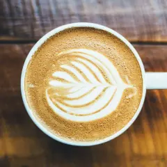 Un cappuccino con latte art su un tavolo di legno. Chissà chi ha inventato il cappuccino, ma questa tazza è perfetta.