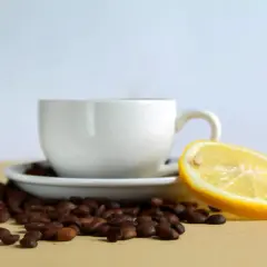 Tazzina di caffè con chicchi sparsi e una fetta di limone, un contrasto di sapori per iniziare la giornata.