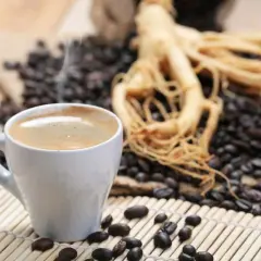 Tazza di caffè fumante accanto a chicchi tostati e radice di ginseng, che contiene caffeina per un risveglio energico.