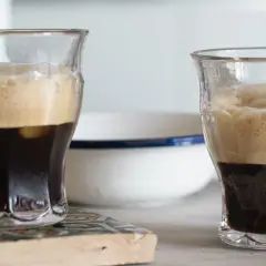 Due bicchieri di caffè shakerato cremoso, con la schiuma dorata che sovrasta il caffè scuro. Uno ha un cucchiaino.