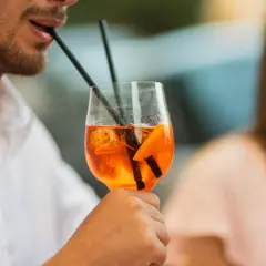 Un uomo sorseggia un Aperol Spritz, perfetto per la sua aperitivo ricetta. Ghiaccio e arancia completano il drink.