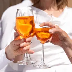 Tre mani brindano con bicchieri di Aperol, un drink rinfrescante e senza glutine, sotto il sole.