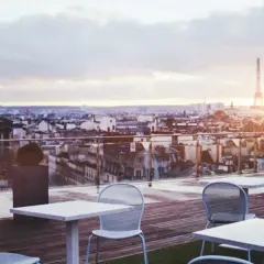 Terrazza con vista su Parigi al tramonto, tavoli e sedie vuoti, la Torre Eiffel sullo sfondo. Un luogo perfetto per godersi i locali storici di Parigi.