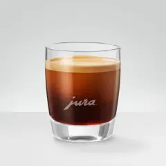 Un bicchiere di vetro con un doppio macchiato, la schiuma dorata corona il caffè scuro. Il logo Jura è inciso sul vetro.