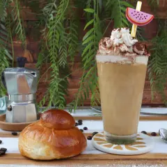 Un bicchiere di caffè freddo siciliano con panna e cacao, accanto a una brioche e una moka.