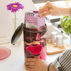 Mano inserisce pacchetto di caffè in una lattina decorata con chicchi e tazzina. Si può congelare il caffè liquido per conservarlo al meglio.