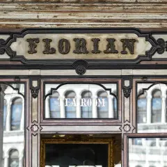 Ingresso del storico **Cafe Florian**, con insegna in rilievo e riflessi di palazzi veneziani nelle vetrate.